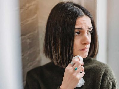 Una mujer mira a través de una ventana con ojos llorosos y un pañuelo en la mano
