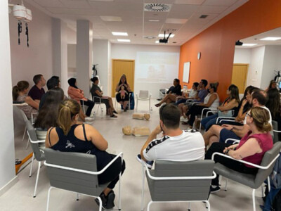 Nos formamos con Cruz Roja en primeros auxilios pediátricos Asistentes al curso de primeros auxilios pediátricos, sentados en torno a dos muñecos para las demostraciones