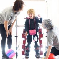 Las terapeutas Irma García y Nerea Meabe ayudan a Danele, de 4 años, a caminar con el exoesqueleto