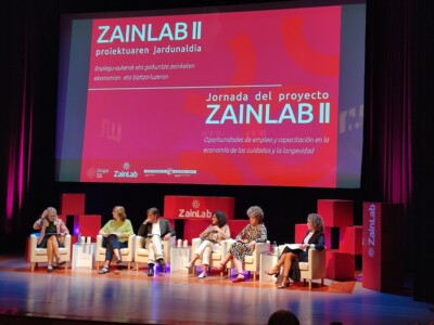 Nerea Gutiérrez: “Que la Atención Centrada en la Persona se incluya en todas las políticas” Varias personas sentadas en un escenario bajo una pantalla en la que se lee el nombre de la jornada