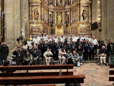 Celebramos con ATECE Gipuzkoa el Día del Daño Cerebral 2023 en Donostia Un grupo de personas, algunas en silla de ruedas, delante de los integrantes del coro Eresmin, con el retablo de la iglesia de San Vicente detrás de ellos