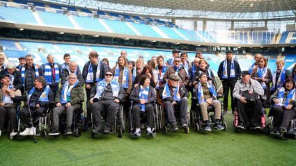Personas usuarias de Aita Menni visitan el Reale Arena con leyendas de la Real Sociedad Un amplio grupo de personas, con bufandas de la Real Sociedad, en el césped del estadio Reale Arena de San Sebastián