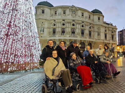 Gabonetako irteerak Bilbon barrena Un grupo de personas mayores, junto a un enorme árbol de Navidad delante del edificio del Teatro Arriaga de Bilbao