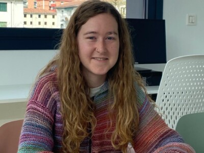 Ile luzea eta koloretako jertsea dituen emakume gazte batek irribarre egiten dio kamerari