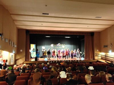 Un salón de actos con un grupo de personas en el escenario y público en las butacas