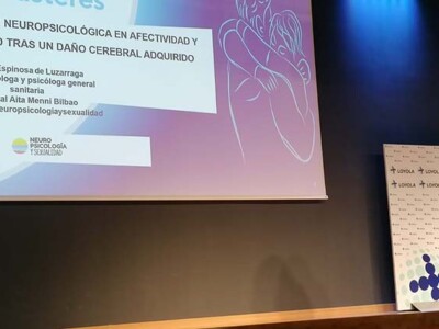 Hablando en la Universidad Loyola de Sevilla sobre salud sexual tras un daño cerebral Ainhoa Espinosa, en un escenario delante de una pantalla con el tíutlo de su ponencia