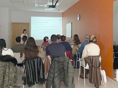 Un grupo de personas en una sala, escuchando a una ponente