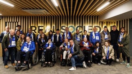 Un amplio grupo de personas posa con bufandas de la Real Sociedad en las instalaciones del estadio Reale Arena