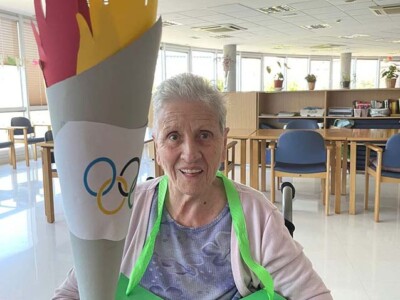 Olinpiaden espirituak Txurdinagabarri Egoitza hartu du Una mujer mayor sostiene una antorcha olímpica hecha de cartulina de colores