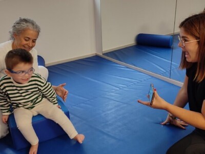 La fisioterapeuta Irma García sostiene en su regazo a Danel, que mira hacia un móvil que sostiene su madre