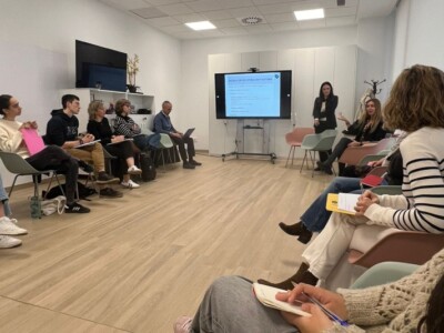 Varias personas sentadas en una sala en la que hay una pantalla