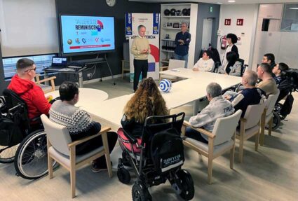 Varias personas sentadas alrededor de una mesa frente a una pantalla