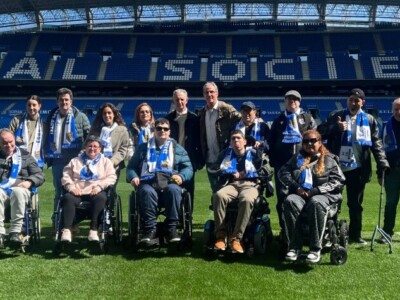Un grupo de personas, con bufandas de la Real Sociedad, en el césped del estadio de Anoeta
