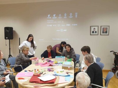 Actividades intergeneracionales en Txurdinagabarri con los colegios Berriotxoa y Begoñazpi Varias personas jóvenes y mayores, en torno a una mesa llena de materiales para manualidades