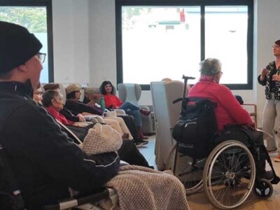 La guía "Quiero que sepas...", presentada en Musakola Un grupo de personas mayores sentadas atiende las explicaciones de una mujer, de pie, delante de una pantalla