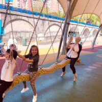 Un niño, una niña y iuna mujer mayor, en un balancín de un parque