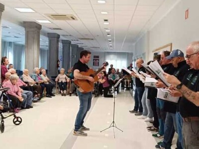 Txoko Gurea Abesbatza "se estrena" en la Residencia Txurdinagabarri Un coro, junto a un guitarrista, delante de un amplio grupo de personas mayores sentadas
