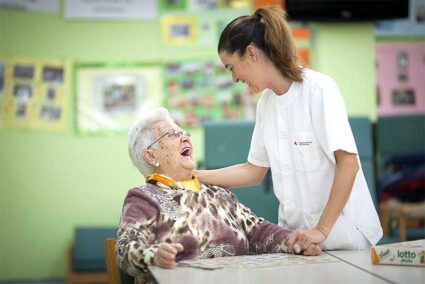Una mujer mayor sentada y una profesional con bata blanca, riéndose