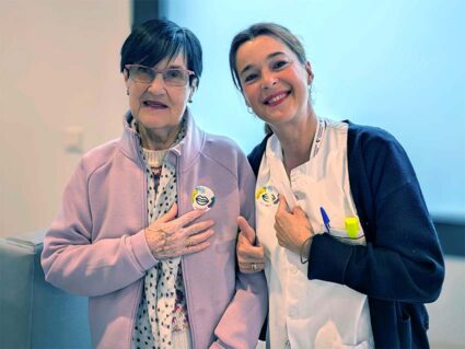 Una mujer mayor y otra joven con uniforme sanitario muestra sus chapas de la campaña Euskaraldia