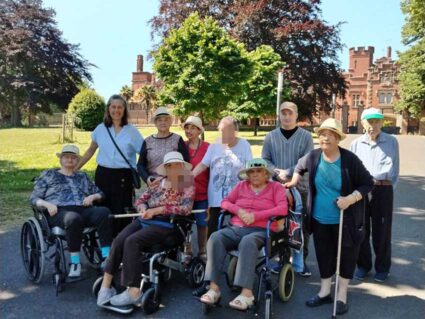 Un grupo de personas mayores, algunas en silla de ruedas, ante el un edificio señorial