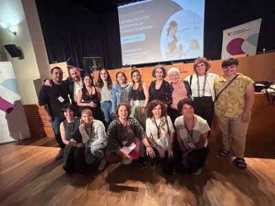 Un grupo de 15 personas, dos hombres y el resto mujeres, fotografiados dlante de un escenario en el que se ven logotipos de la Fundación Hospitalarias