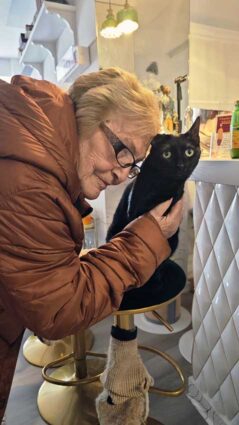 Una mujer mayor acaricia a un gato que está sobre una banqueta