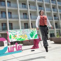 Un dantzari se eleva del suelo ante un crtel en el que se lee "20 años" en euskera