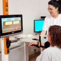 Una paciente con daño cerebral, usando el robot de rehabilitación del miembro superior Diego con ayuda de una terapeuta