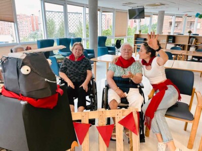 Txurdinagabarri gorriz eta zuriz jantzi zen berriro Dos personas mayores y una joven, con pañuelos rojos, posan junto a un toro y una valla de cartón