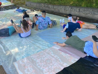 Varios jóvenes se deslizan tumbados sobre una superficie de plástico mojada