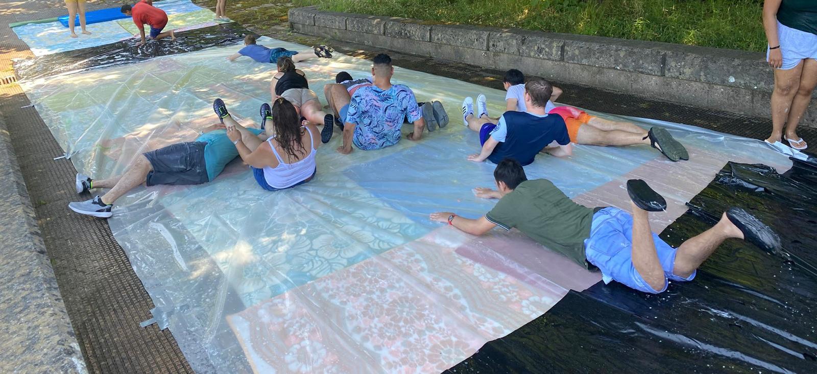 Udako festa ospitalean: egun freskagarri bat ur jolasen artean Gazte batzuk plastikozko gainazal busti baten gainean txirrist egiten