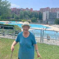 Una mujer mayor posa delante de unas piscinas al aire libre