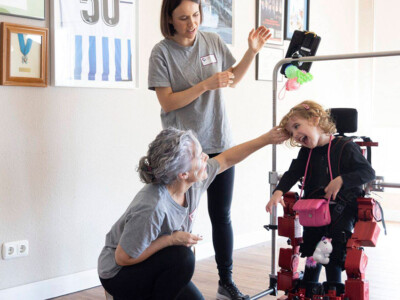 Una niña participante en el proyecto, utilizando el exoesqueleto junto a Inma García y Nerea Meabe