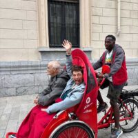 Dos personas sentadas en la parte delantera de un triciclo de Cruz Roja