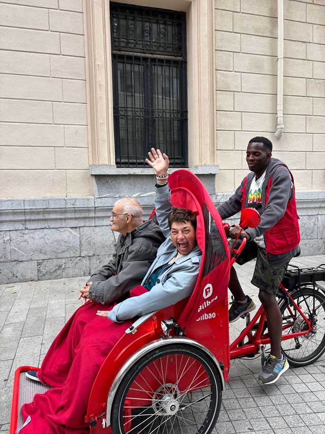 Hiria bizikletaz zeharkatzen Dos personas sentadas en la parte delantera de un triciclo de Cruz Roja