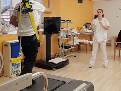Un hombre calanza una pelota a una fisioterapeuta mientras camina en una cinta de marcha