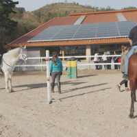 Una mujer y un hombre montan a caballo en la pista de un centro hípico durante una sesión de equinoterapia