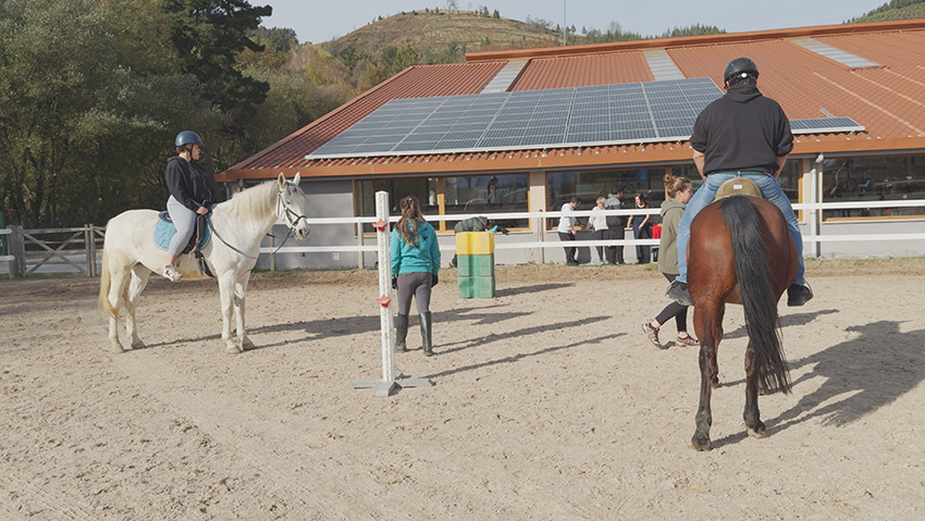 Equinoterapia en enfermedad mental y discapacidad intelectual: beneficios de la terapia asistida con caballos Una mujer y un hombre montan a caballo en la pista de un centro hípico durante una sesión de equinoterapia