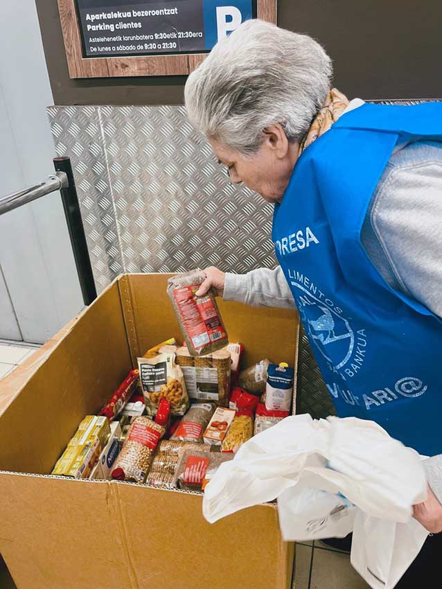 En la Gran Recogida del Banco de Alimentos de Bizkaia Una mujer mayor con un chaleco de voluntaria coloca alimentos en una caja