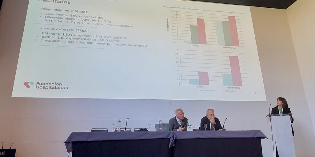 Una mujer habla desde un atril en presencia de dos hombres sentados en una mesa
