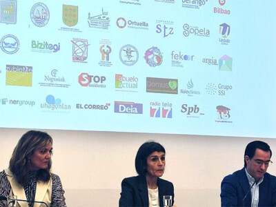 Dos mujeres y uun hombre, delante de una pantalla con logotipos