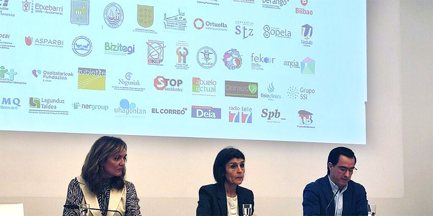 Bi emakume eta uun gizon, logotipoak dituen pantaila baten aurrean